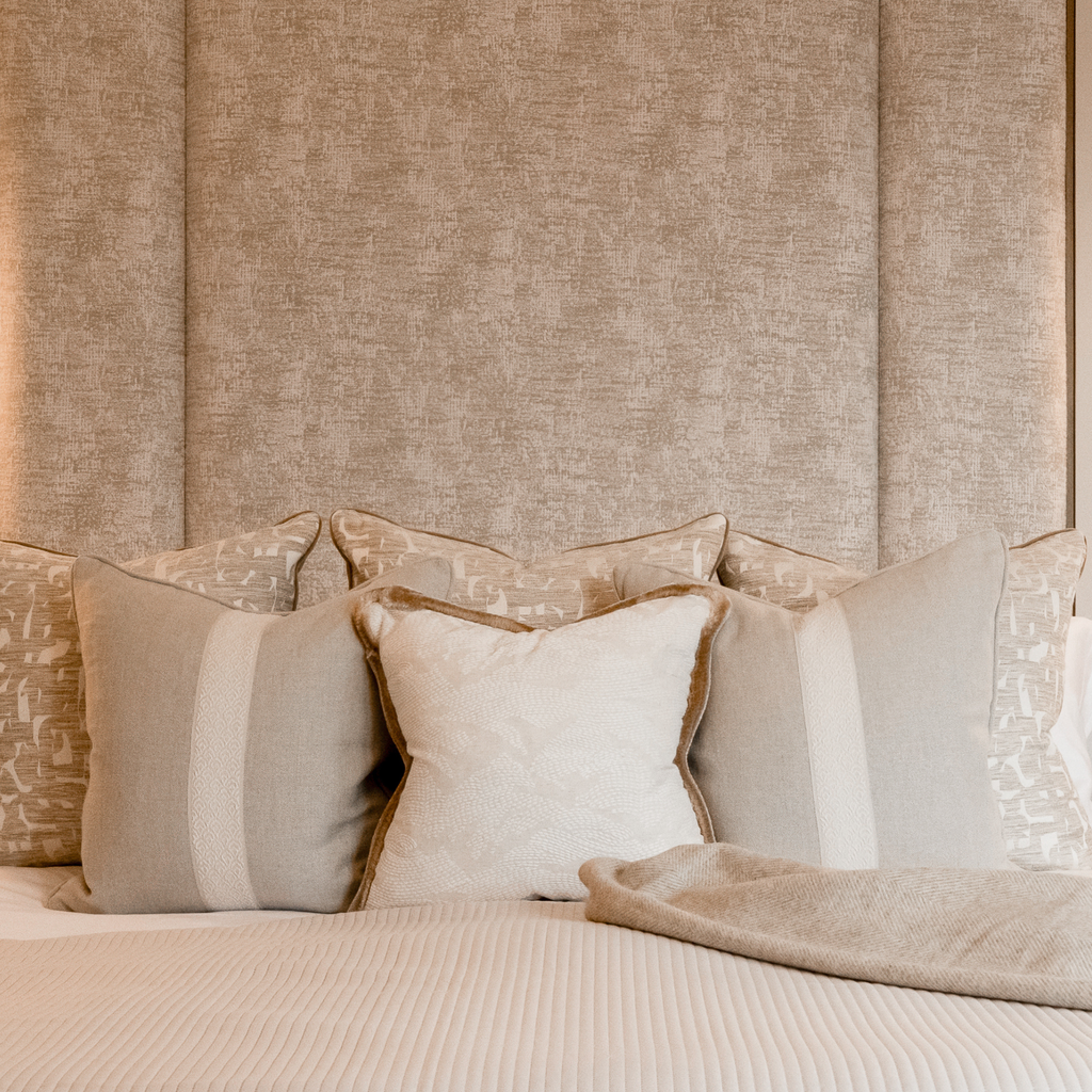 Neatly arranged neutral cushions on a bed with a textured wall in the background