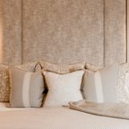 Neatly arranged neutral cushions on a bed with a textured wall in the background