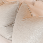 Close-up of beige textured cushions layered on a bed.