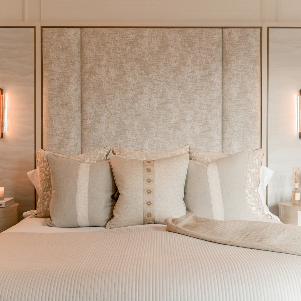 Neatly made bed with decorative cushions against a textured headboard in a bedroom setting.