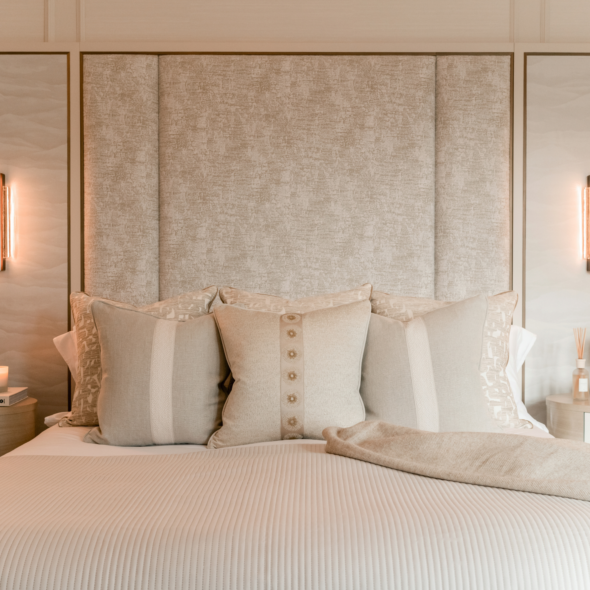Neatly made bed with decorative cushions against a textured headboard in a bedroom setting.