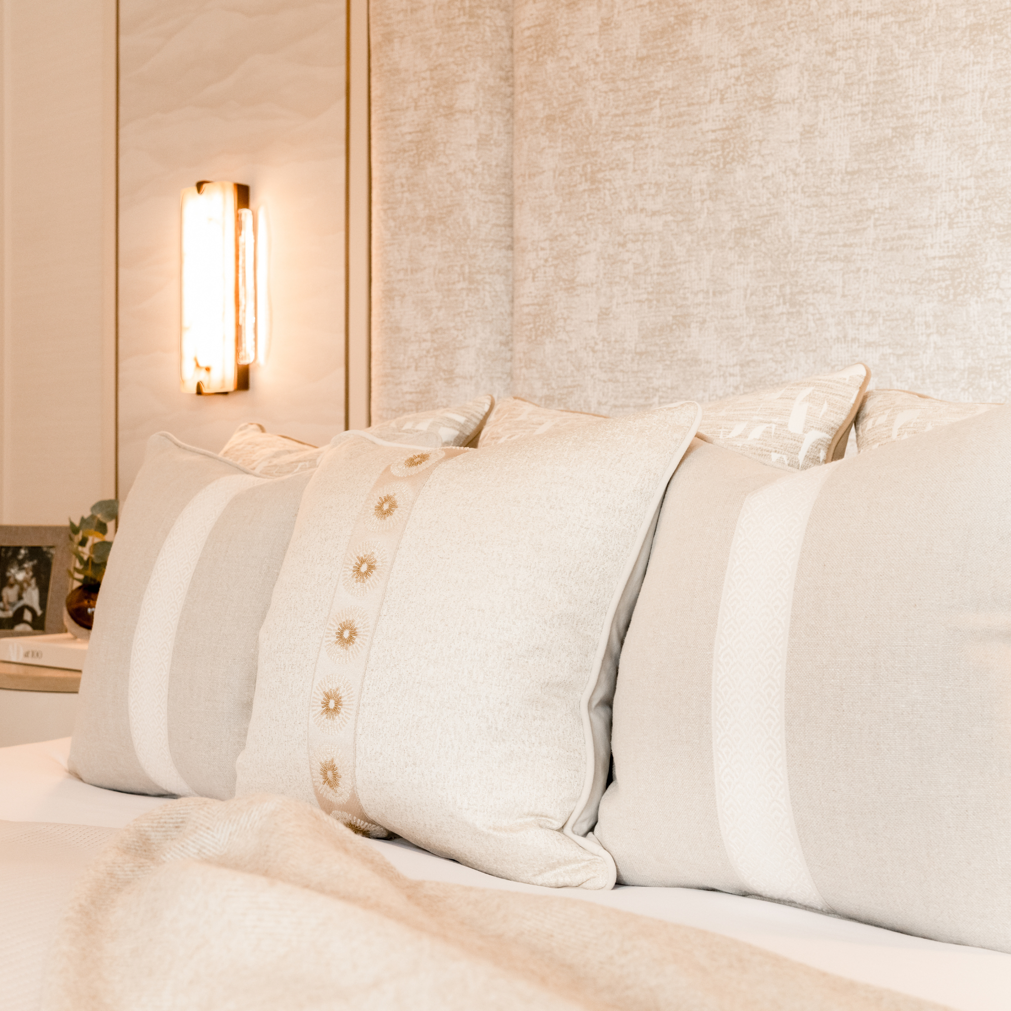 Neatly arranged neutral cushions on a bed with a decorative headboard and ambient lighting.