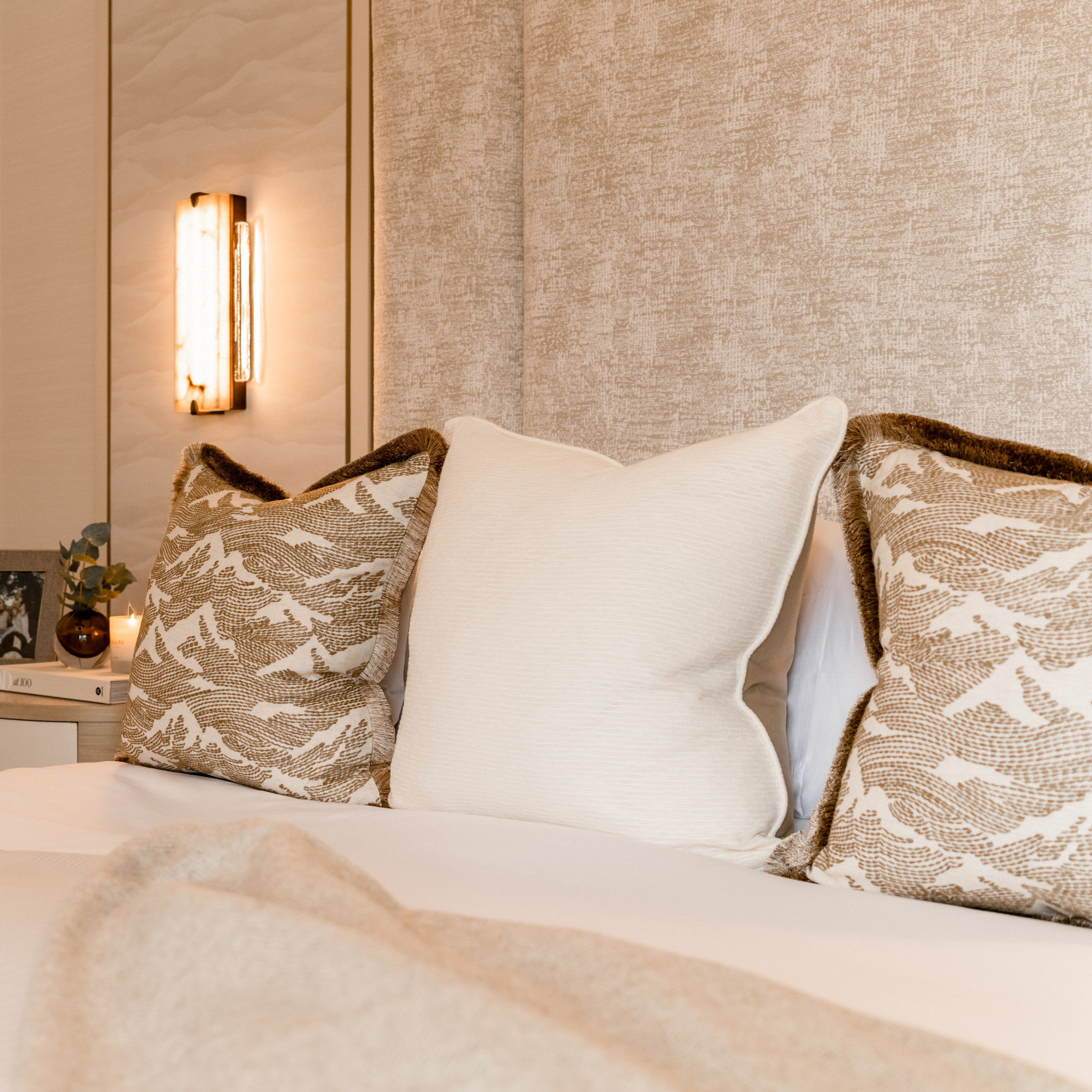 Decorative neutral cushions layered on a bed with ambient lighting in the background