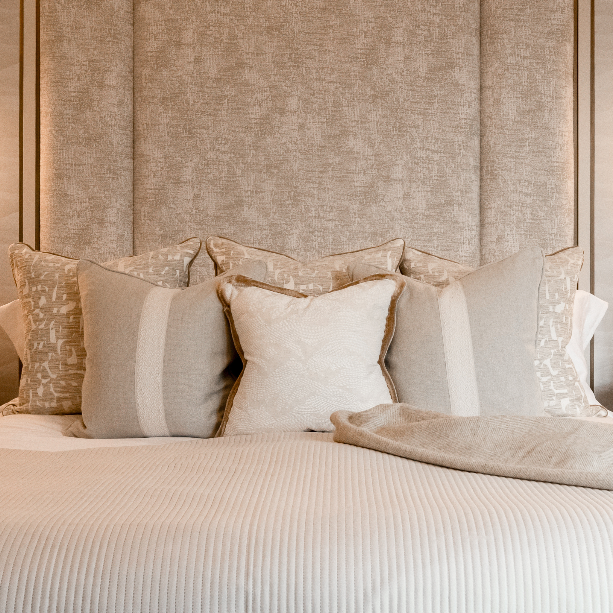 6 neatly arranged neutral cushions on a bed with a textured headboard