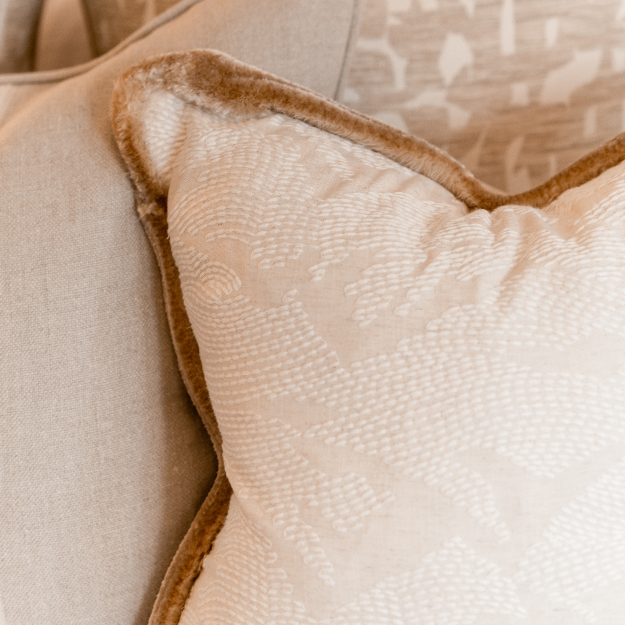 Close-up of a cushion featuring a textured off-white fabric and a luxurious gold velvet piping trim.