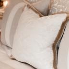 Close-up of a cushion featuring off-white textured fabric and a gold velvet fringe trim.