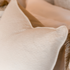 Close-up of a textured fabric off-white cushion layered against beige headboard.