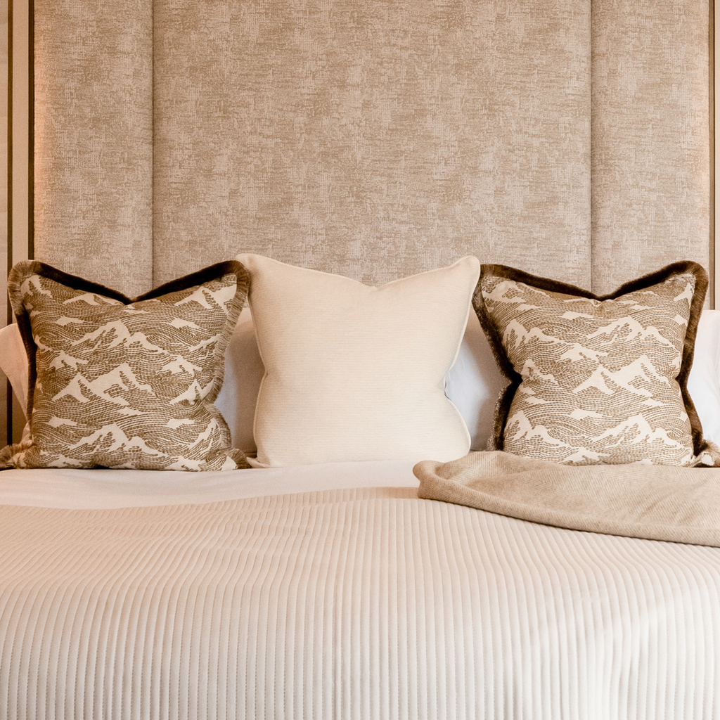 Neatly arranged neutral cushions on a bed with a textured headboard.