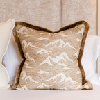 Decorative cushion with a gold and ivory intricate pattern and gold fringing styled on a white bed.
