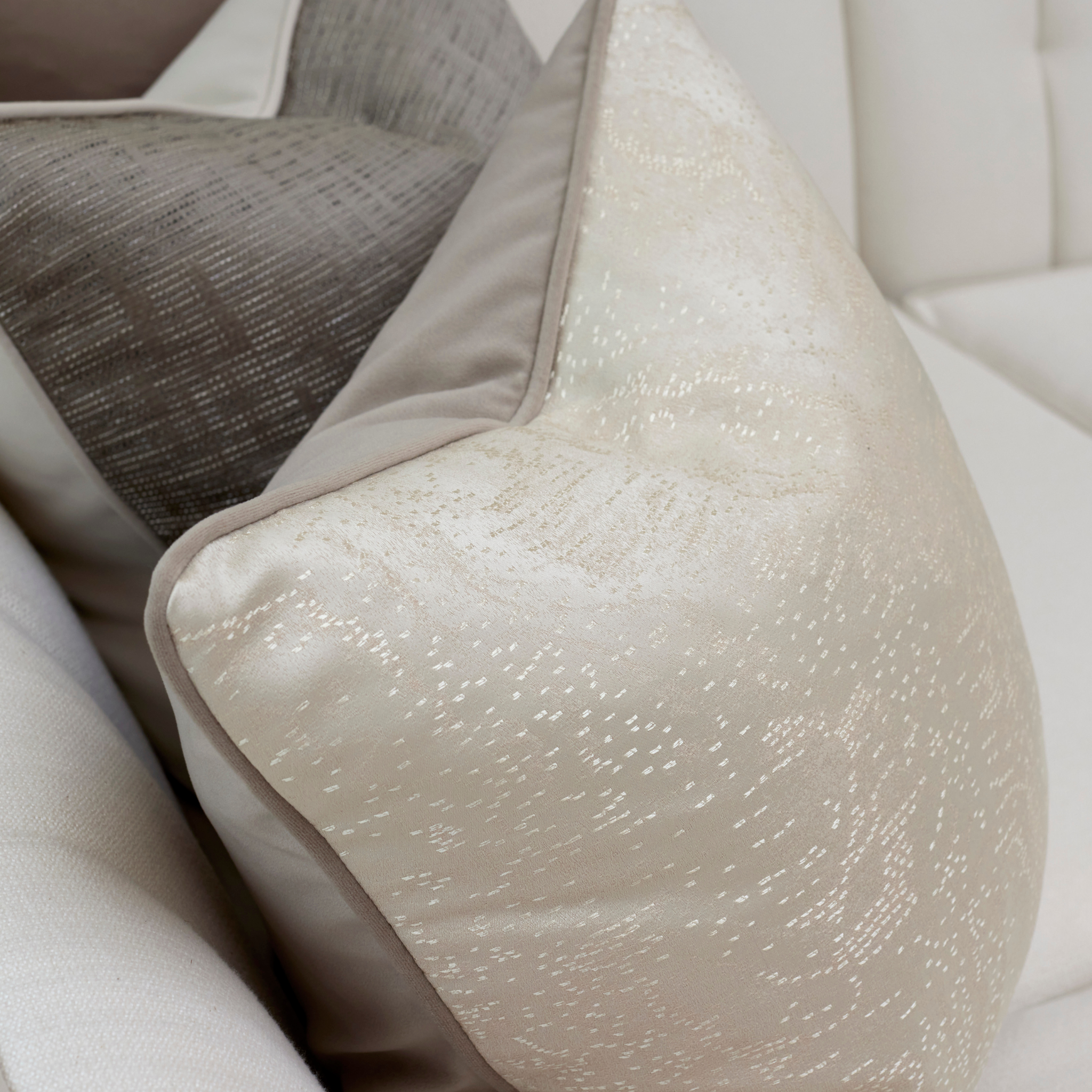 Close-up of a luxurious ivory cushion with a textured metallic finish, layered on a white sofa.