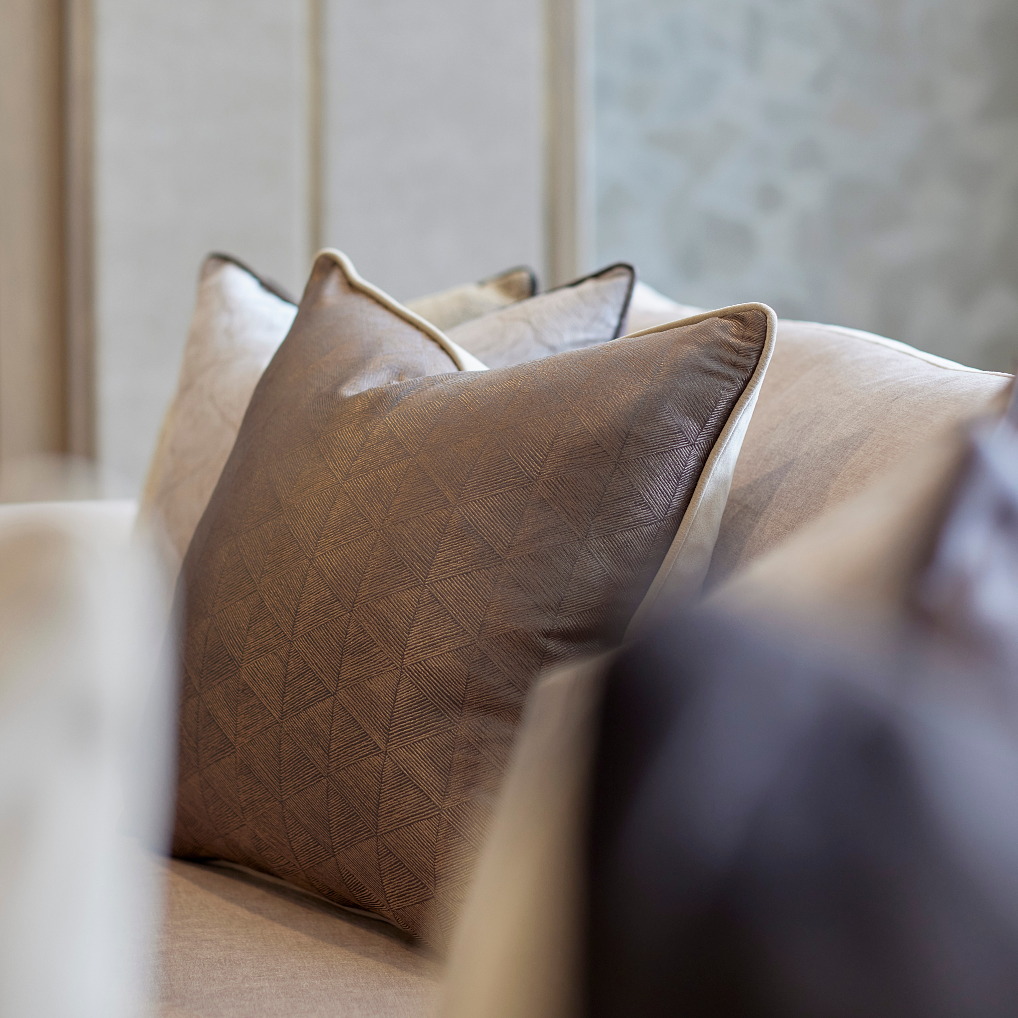 Brown metallic textured statement cushion styled on a beige sofa with a blurred photography effect